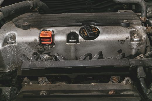 Grimy engine valve cover and oil cap on a vehicle that has gone too long between oil changes