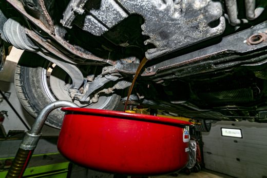 Used engine oil draining out of the drain plug into a red catch pan