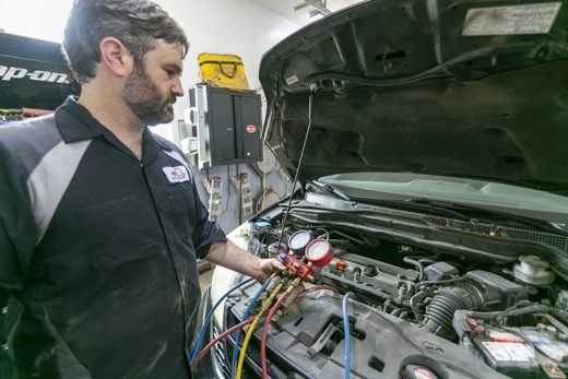 Auto Solve technician servicing a vehicle A/C system with manifold gauges