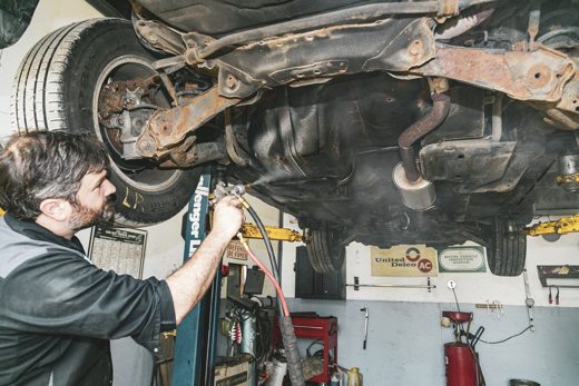 Technician spraying undercoating across a vehicle underbody