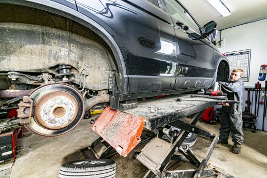 Auto Solve mechanic inspecting a raised SUV on the lift during a pre-trip check
